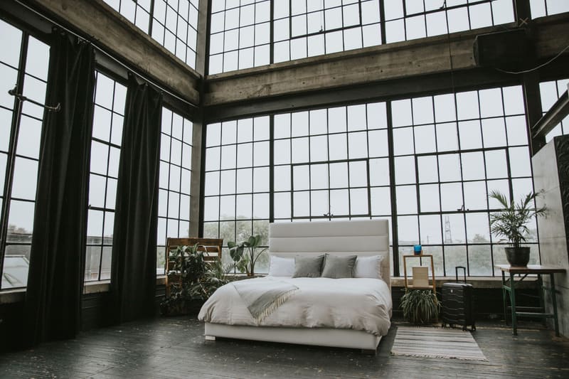 The Zazen Bed made up with a grey throw, in a loft with floor-to-ceiling windows