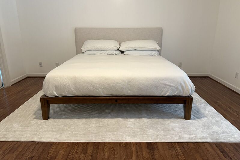 A finished upholstered headboard in an oat fabric on a walnut platform bed with white bedding