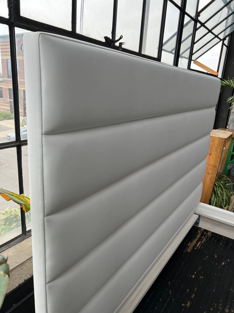 A horizontal channel headboard in white vegan leather, before it is joined to the platform
